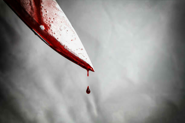 close-up of man holding knife smeared with blood and still dripping.