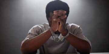 African American young man wearing handcuffs crying in remorse as criminal arrested, copy space