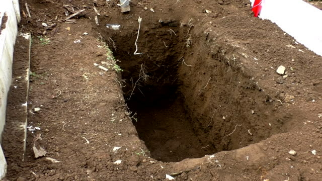 Zoom in on recently dug empty grave in the graveyard