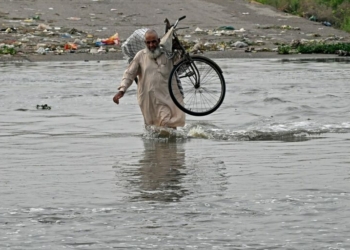 A man carries his bicycle as he wades along a flooded road after heavy monsoon rains in Karachi on August 20, 2025. More than 20 people died in a fresh spell of deadly monsoon rain in Pakistan, National Disaster Management Agency (NDMA) said on August 20. (Photo by Rizwan TABASSUM / AFP)