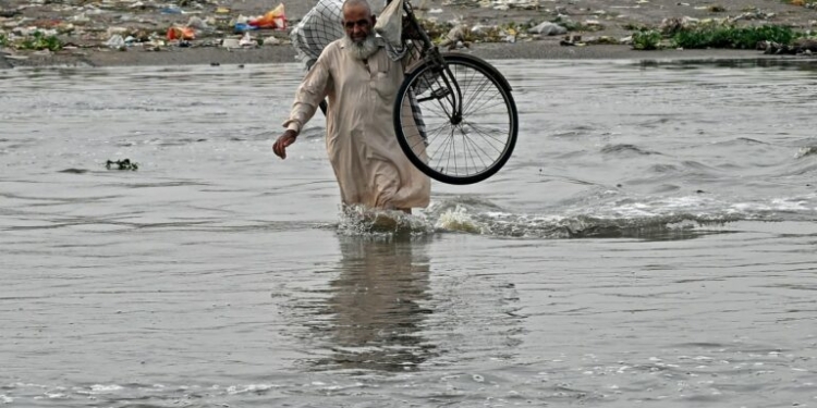 A man carries his bicycle as he wades along a flooded road after heavy monsoon rains in Karachi on August 20, 2025. More than 20 people died in a fresh spell of deadly monsoon rain in Pakistan, National Disaster Management Agency (NDMA) said on August 20. (Photo by Rizwan TABASSUM / AFP)