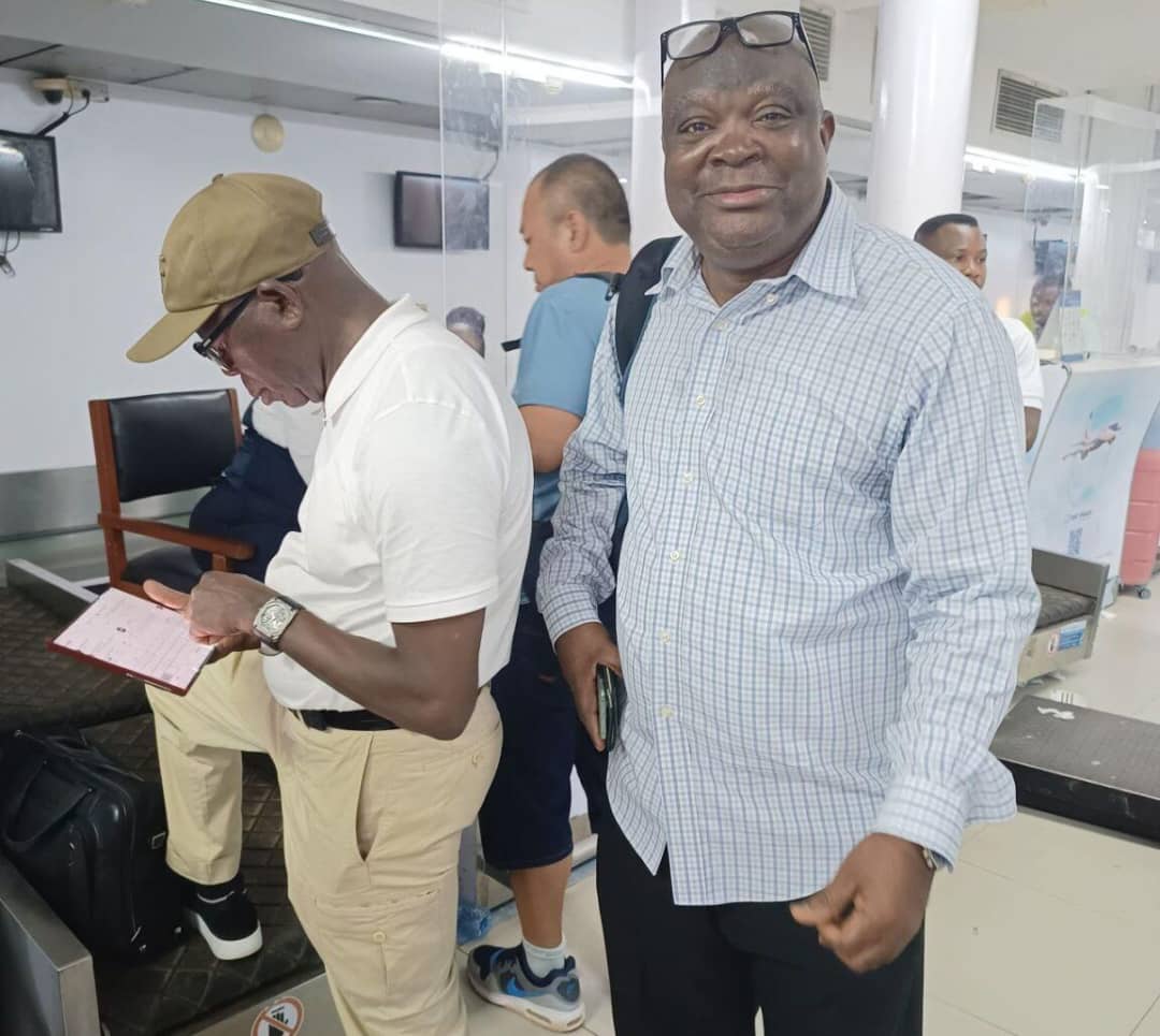 Oshiomhole, in a brown baseball cap, standing at the Air Peace check-in counter