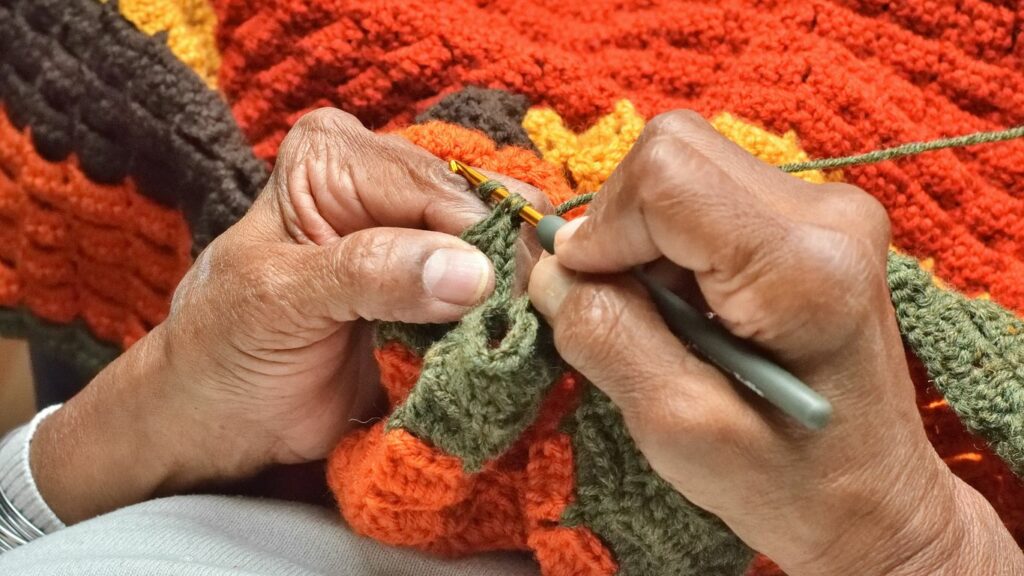 A person knitting a blanket with a pair of scissors