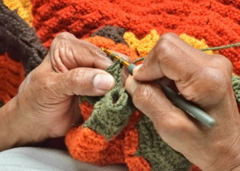 A person knitting a blanket with a pair of scissors