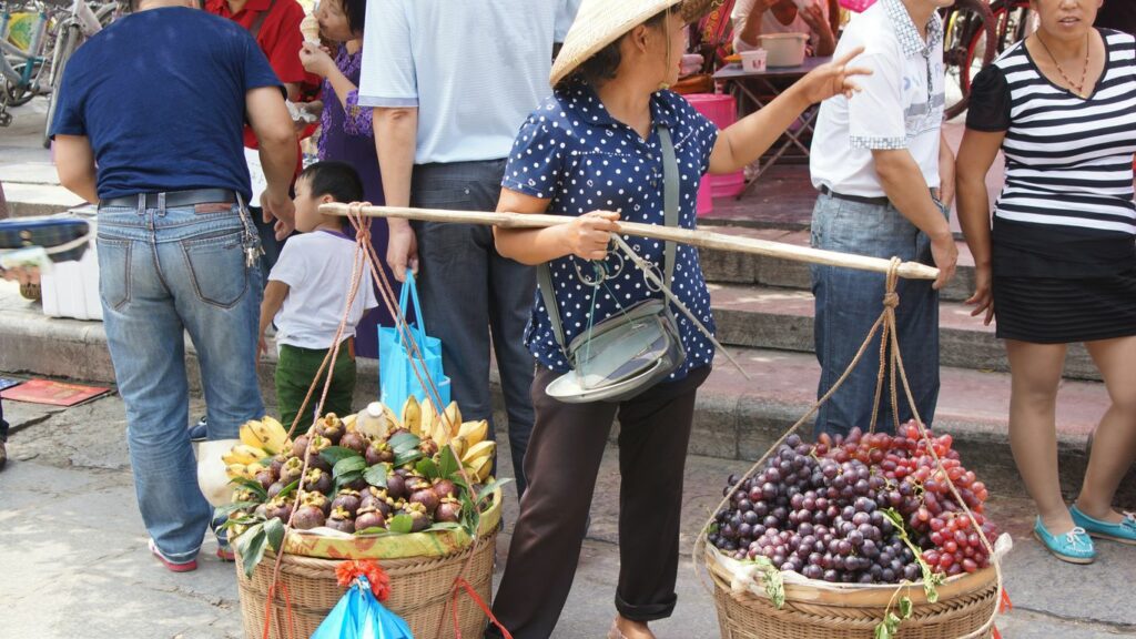 Woman carries fruit through a crowded market.
