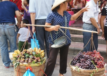 Woman carries fruit through a crowded market.