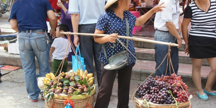Woman carries fruit through a crowded market.