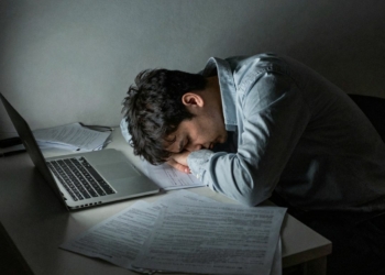 Exhausted person slumped over a desk in a dark room.