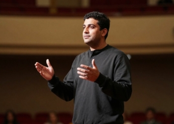 Person speaking confidently on a stage with gestures.