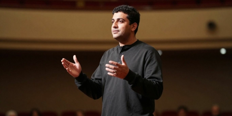 Person speaking confidently on a stage with gestures.